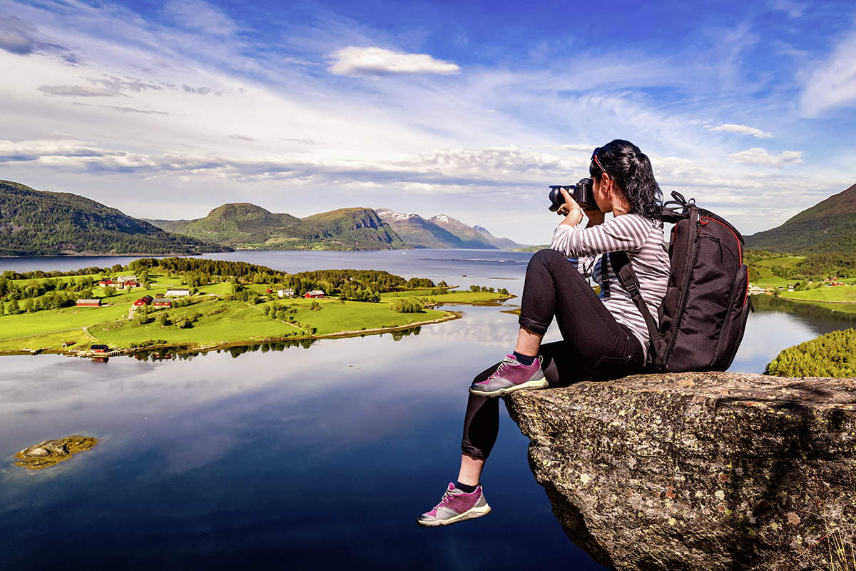 Frau sitzt auf Felsen am Fjord und macht Fotos